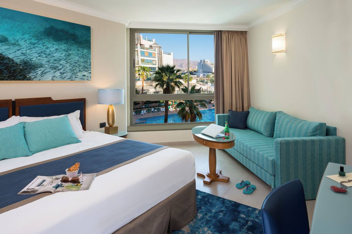 Une chambre d’hôtel avec un lit, un canapé, une petite table et une vue sur une piscine et des immeubles.