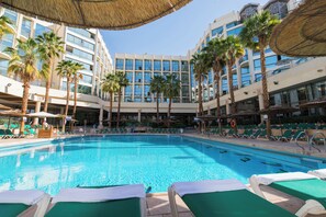 Ein Hotelpool mit Liegestühlen, Palmen und einem Gebäude mit mehreren Balkonen.
