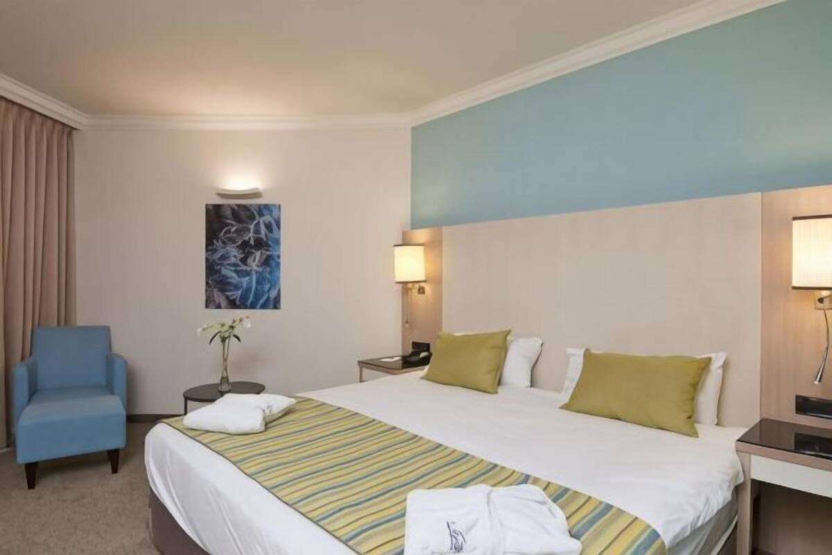 Une chambre d’hôtel avec un lit, une chaise, une table de chevet, une lampe et un tableau au mur.