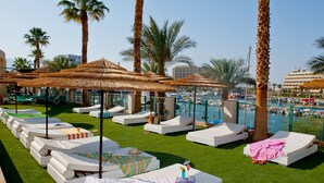 A poolside area with lounge chairs, umbrellas, and a view of the marina. - U Magic Palace (Eilat)