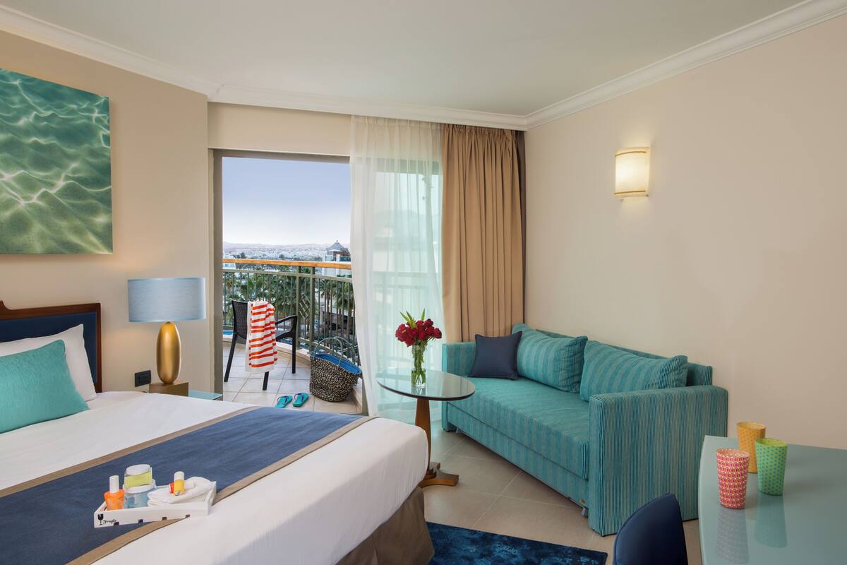 Une chambre d’hôtel comprenant un lit, un canapé, une petite table, une chaise, un balcon avec vue et un luminaire fixé au mur.