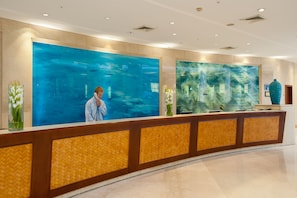 Una recepción con un amplio ventanal, una recepcionista y un jarrón decorativo.