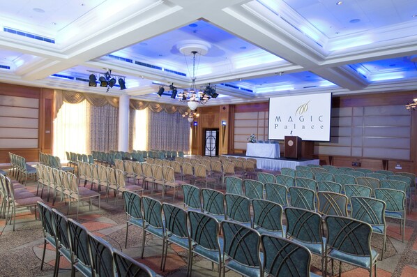 Ein Konferenzraum mit Reihen von Stühlen, einer Bühne mit Rednerpult und einem Banner mit der Aufschrift 'MAGIC Palace'.