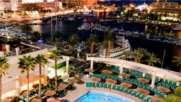 A large indoor swimming pool with multiple lanes, surrounded by lounge chairs and palm trees. - U Magic Palace (Eilat)
