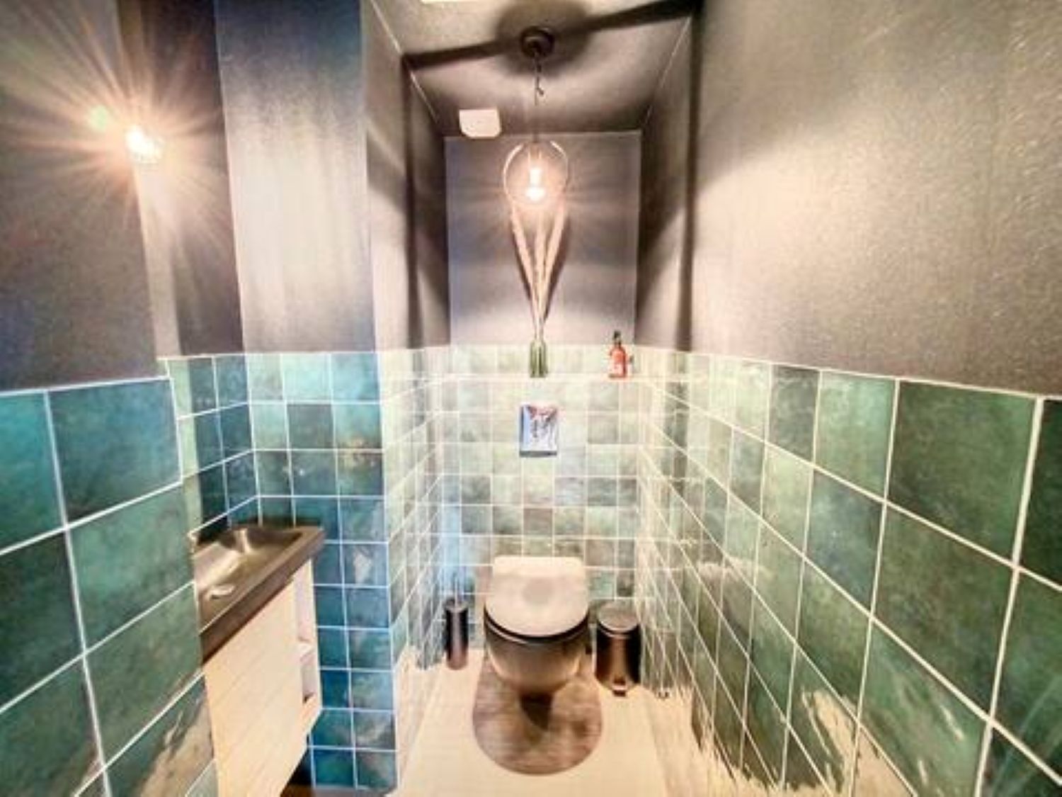 Une petite salle de bain étroite, avec des toilettes, un lavabo et des murs carrelés.