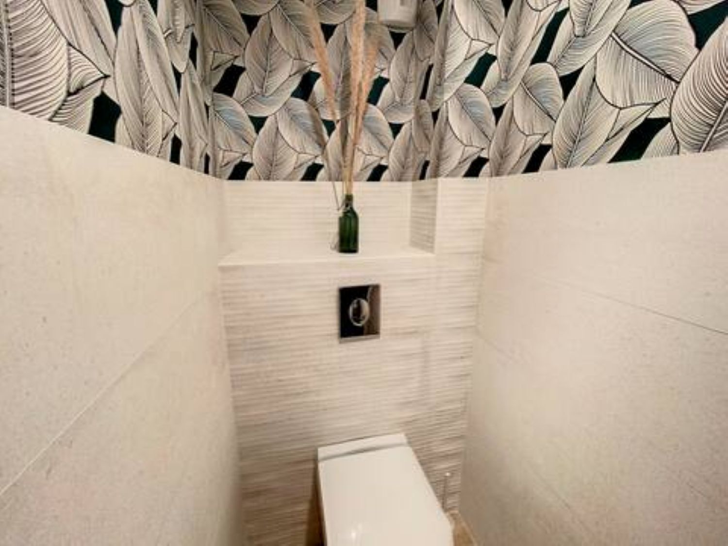 A bathroom with a white toilet, a green vase on a shelf, and a patterned wall.