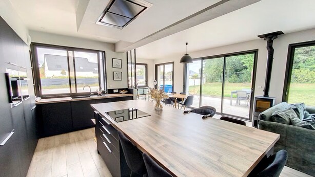 Une cuisine moderne dotée d’un grand îlot central, de meubles de rangement noirs et d’un coin repas avec une table et des chaises.