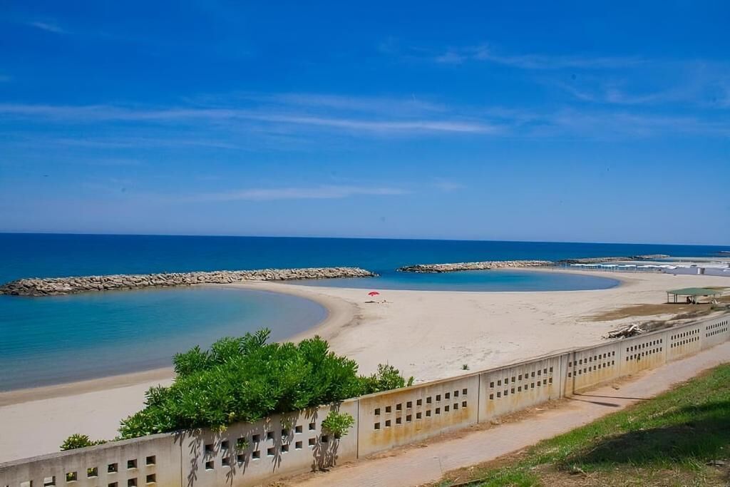 Une plage au rivage incurvé, une plage de sable fin et un ciel bleu clair.