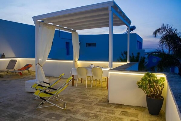 A rooftop terrace with a covered seating area, a dining table, and a potted plant.