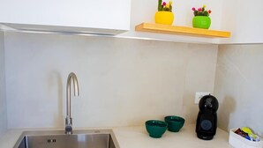 Een moderne keuken met een roestvrijstalen spoelbak, een koffieapparaat en twee kleine groene schaaltjes op het aanrecht.