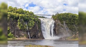 A waterfall cascading over a cliff into a river, with a bridge in the background.