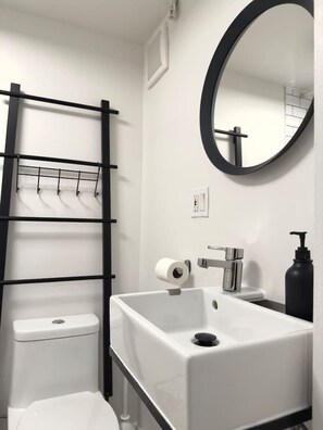 A bathroom with a white sink, a black faucet, a black soap dispenser, a toilet, and a black towel rack.