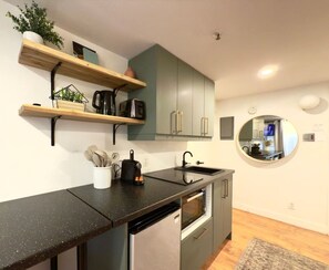 A modern kitchen with a black countertop, stainless steel appliances, and wooden shelves. - Lovely, centrally located, modern, and well-appointed loft. (Québec)