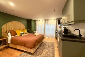Une chambre moderne avec un grand lit, une table de chevet et un coin cuisine intégré avec un évier.