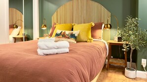 Ein Schlafzimmer mit einem Bett, Kissen, einem Nachttisch, einer Lampe und einer Zimmerpflanze.