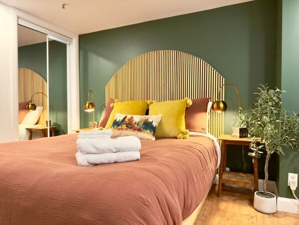 Une chambre à coucher avec un lit, des oreillers, une table de chevet, une lampe et une plante en pot.
