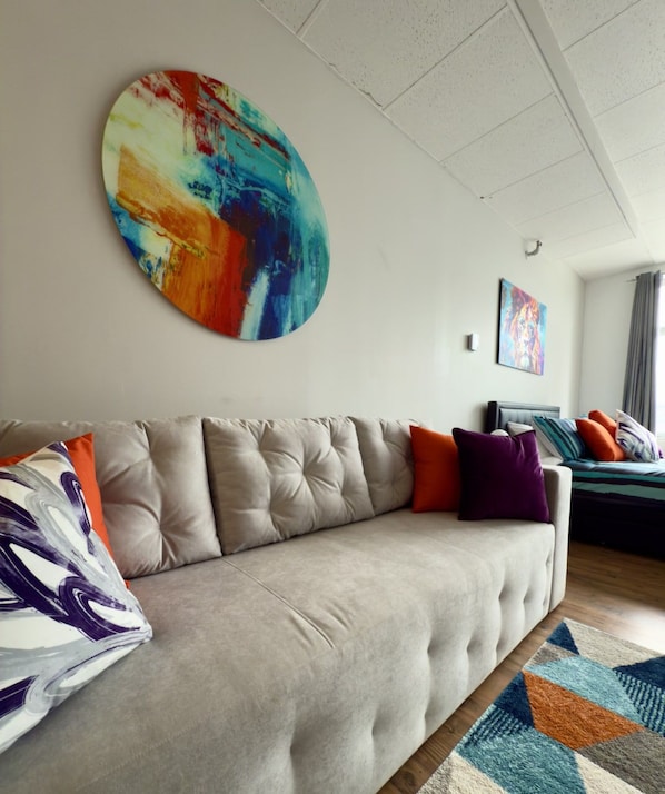 A modern living room with a tufted sofa, colorful abstract art, and a patterned rug.