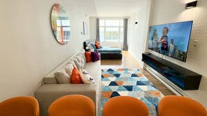 Un salon moderne avec un canapé, des fauteuils, un téléviseur et un tapis à motifs.