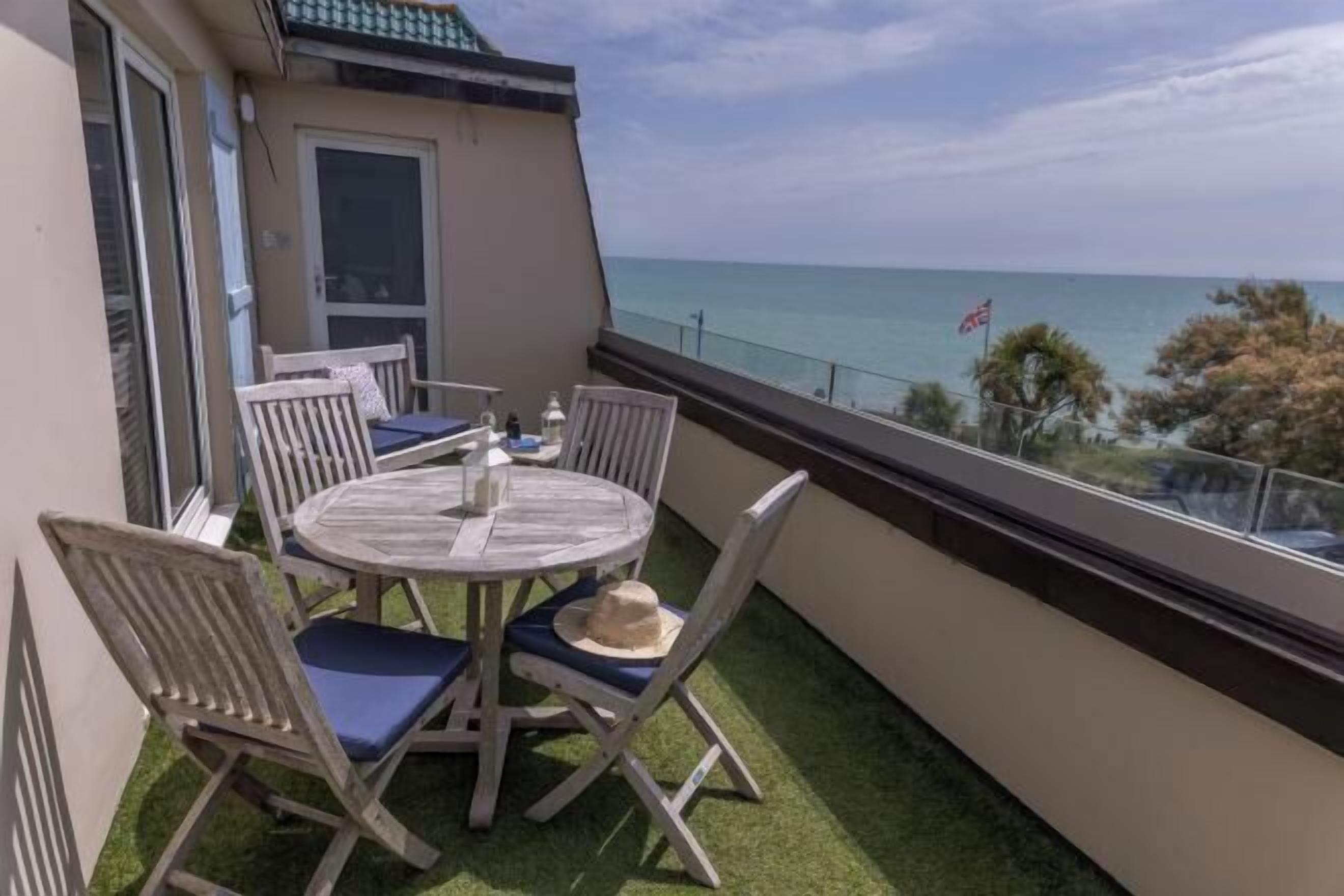 A balcony with a table and chairs, a view of the sea, and a flag.