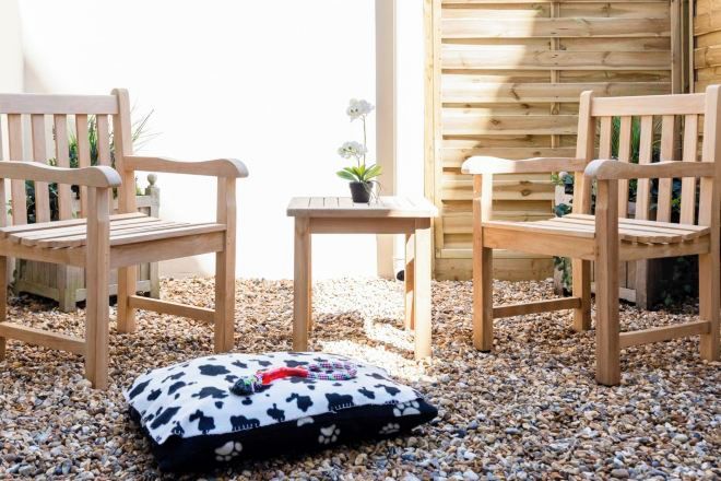 Two wooden chairs and a small table with a cushion on a gravel surface.
