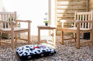 Two wooden chairs and a small table with a cushion on a gravel surface.