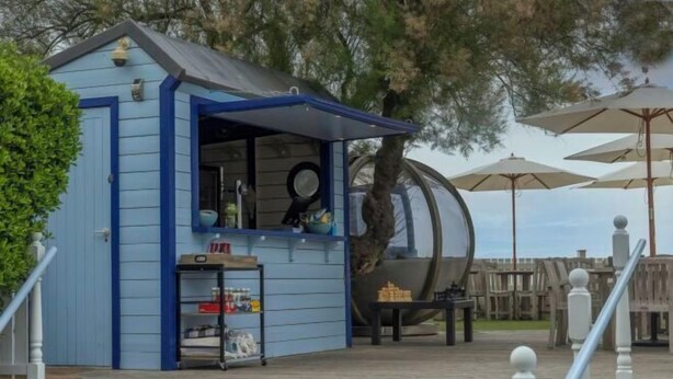 A small blue building with a counter, possibly a snack bar, next to a large cylindrical structure, likely a water slide, with outdoor seating and umbrellas. - Beachcroft Hotel, BW Signature Collection by Best Western (Felpham)