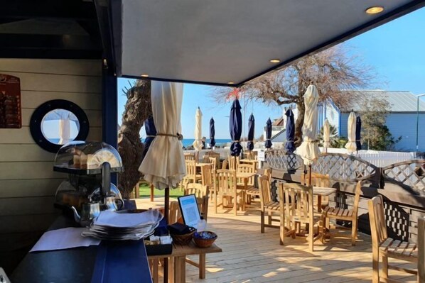 An outdoor seating area with tables and chairs, umbrellas, and a view of the sea. - Beachcroft Hotel, BW Signature Collection by Best Western (Felpham)