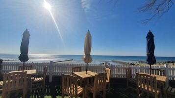 An outdoor seating area with tables and chairs, a white fence, and a view of the ocean.