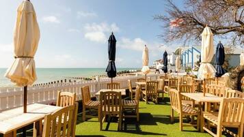 An outdoor seating area with tables and chairs, a view of the sea, and umbrellas.