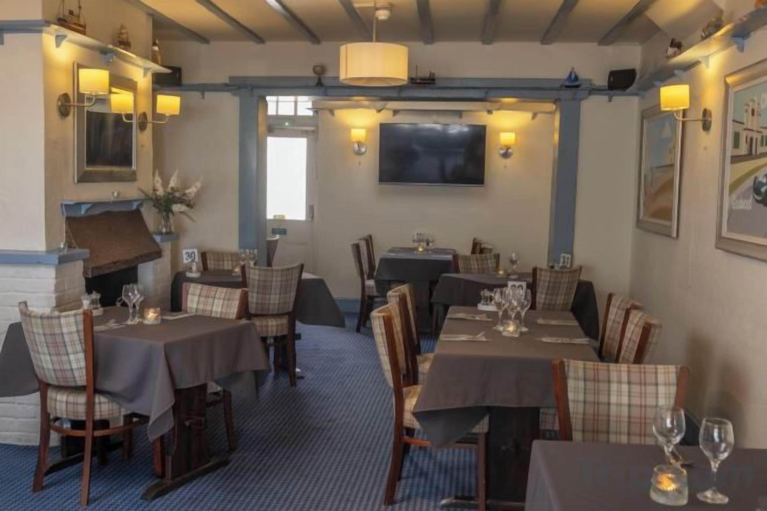 A restaurant with tables set for dining, chairs, and a television mounted on the wall.