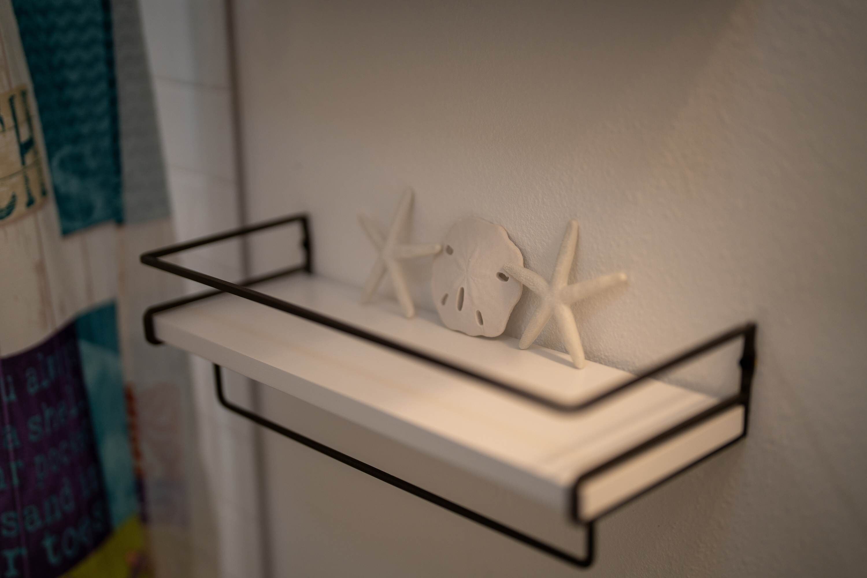A white wall-mounted shelf with a black frame, holding two starfish and a white object.