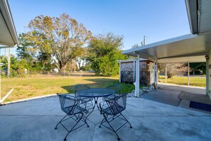 A covered patio with a round table and chairs, a stone wall, and a view of a grassy area with trees. - Break of Dawne (Kissimmee)