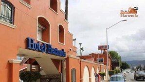 Un hôtel appelé « Hotel Hacienda », avec une enseigne, un trottoir dallé, des voitures garées et une rue en arrière-plan.