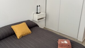 Ein ordentlich bezogenes Bett mit einer dunkel gestreiften Bettdecke, einem senfgelben Kopfkissen und zwei gefalteten Handtüchern.