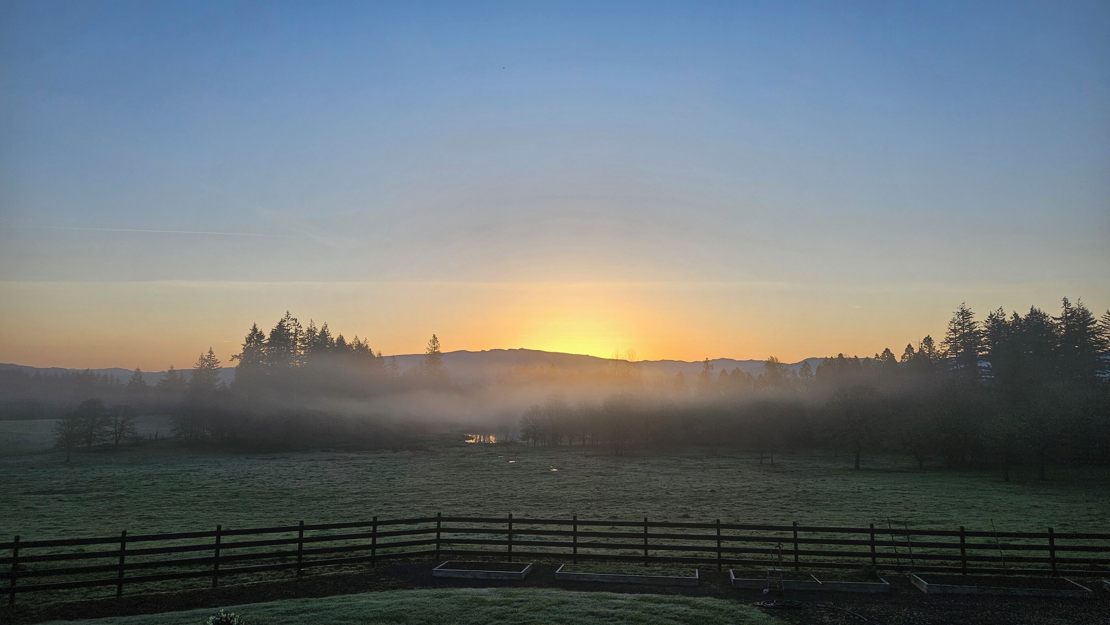 Un amanecer sobre un paisaje brumoso con una valla de madera al frente.