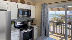 Cocina con gabinetes blancos, microondas, estufa y horno. Hay adornos en la pared y vistas al exterior desde un balcón.