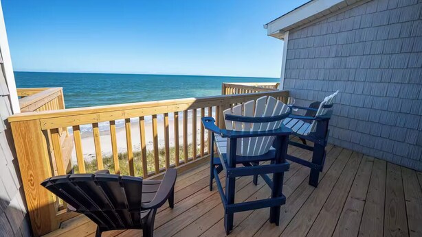 Una terraza de madera con dos sillas Adirondack mirando la playa.