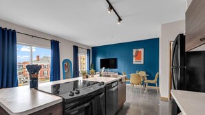 Une cuisine moderne équipée d’une cuisinière, d’un four et d’un lave-vaisselle intégrés. On y trouve un coin repas avec une table et des chaises, ainsi qu’une grande fenêtre agrémentée de rideaux.