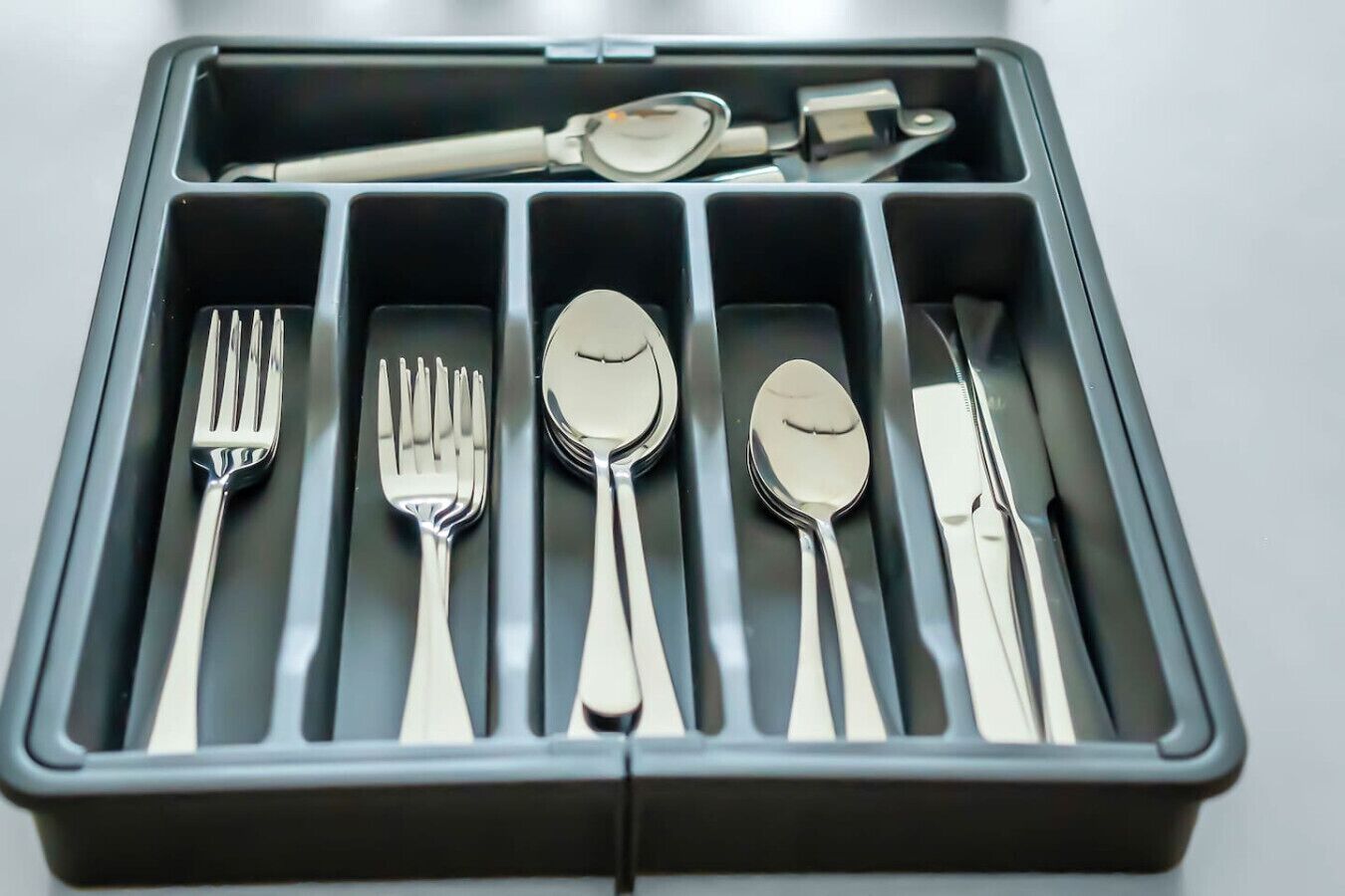 Une trousse de voyage grise, dotée de compartiments contenant une fourchette, un couteau, une cuillère et un repose-cuillère.
