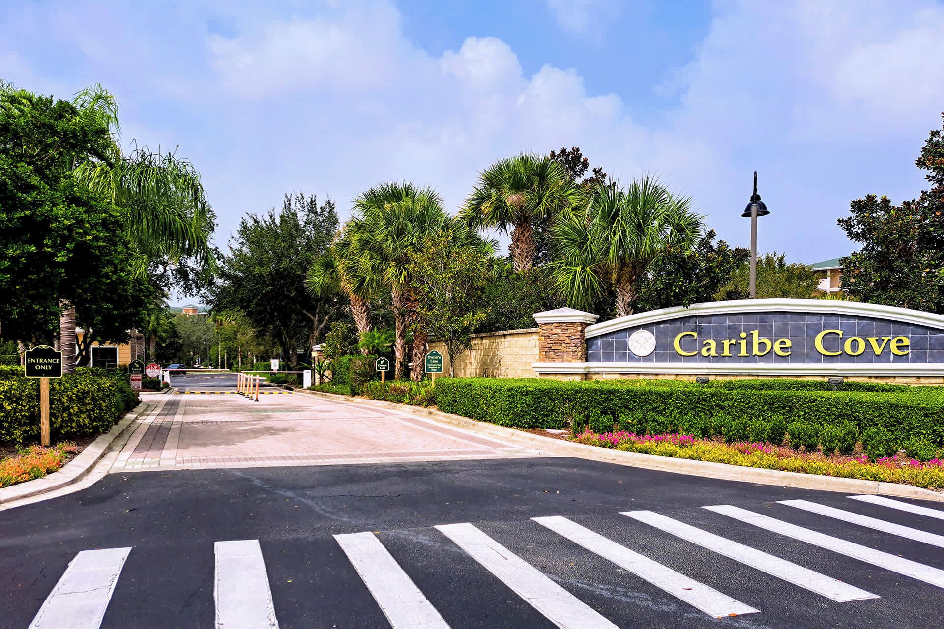 A road leading to a sign for "Caribe Cove" with a pedestrian crossing and lush greenery.