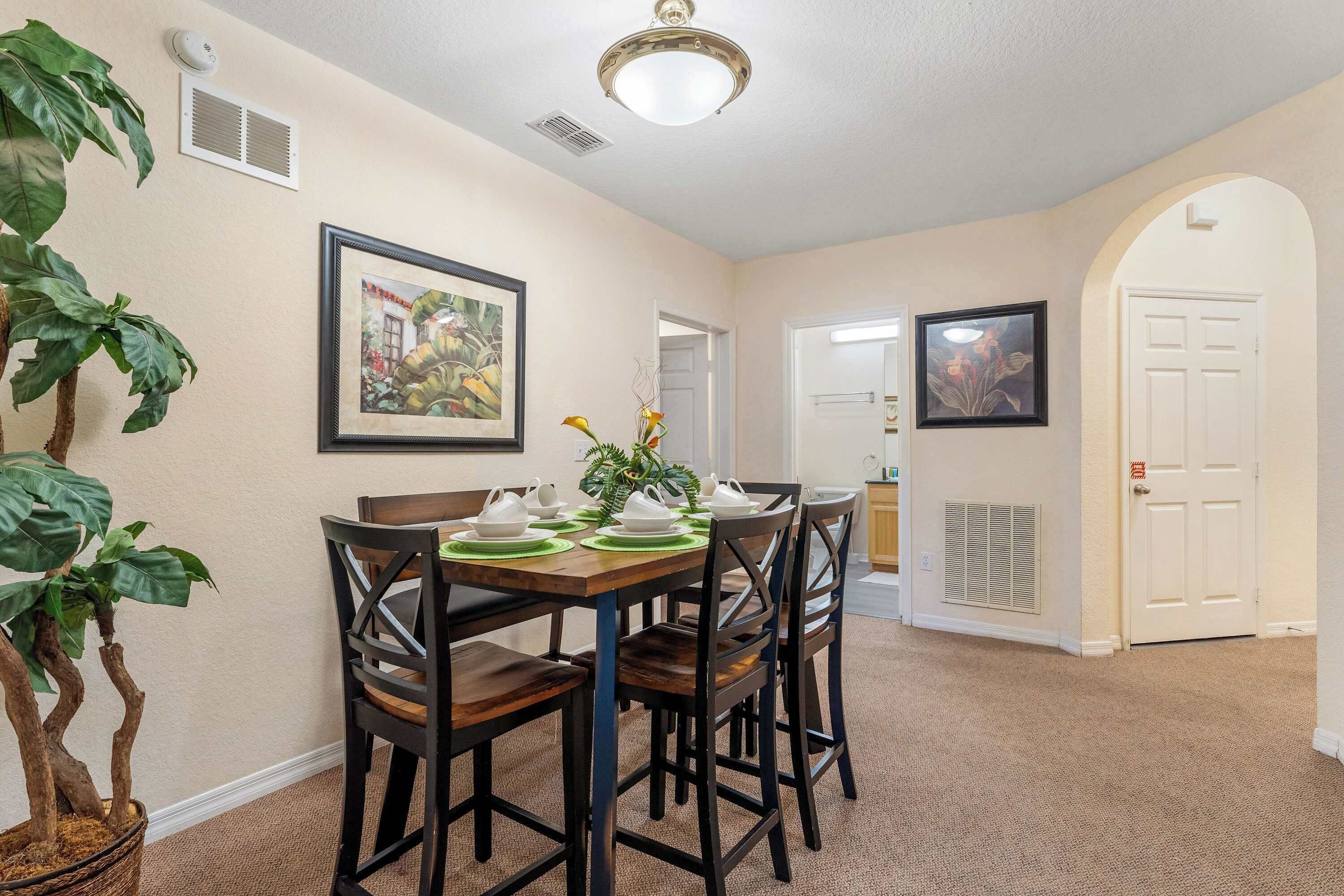 A dining area with a wooden table, four chairs, and a potted plant.
