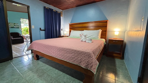 A neatly made bed with a pink quilt, wooden headboard, and two bedside lamps. - Pura Vida Aparment - Downtown La Fortuna (La Fortuna)