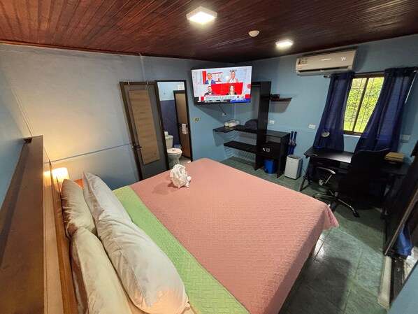 Habitación de hotel con cama, escritorio, silla, televisor y ventana con cortinas.