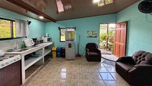 A kitchen with a gas stove, microwave, sink, and a refrigerator. There is a chair and a couch in the living area. - Pura Vida Aparment - Downtown La Fortuna (La Fortuna)
