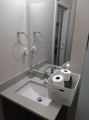 Ein Badezimmer mit Waschbecken, Spiegel, Handtuchhaltern und einem Korb mit Toilettenpapier.