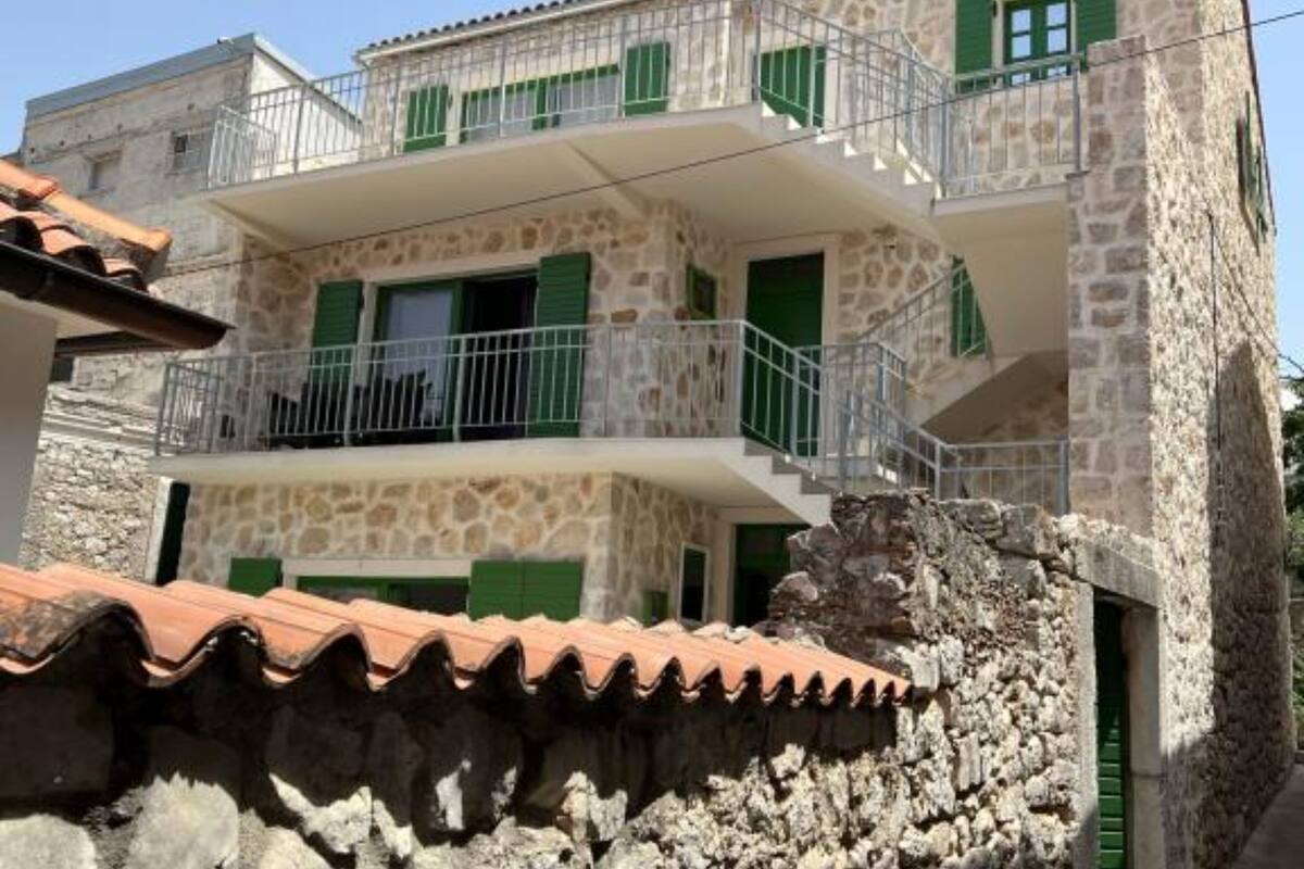 A two-story stone building with green shutters and a balcony.