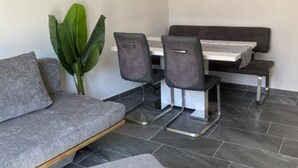 A modern room with a grey sofa, a dining table with chairs, a large green plant, and a flat-screen TV mounted on the wall. - Apartments Stone House Murter (Murter-Kornati)