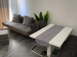 A modern living room with a grey sofa, a white dining table, and a small side table. - Apartments Stone House Murter (Murter-Kornati)