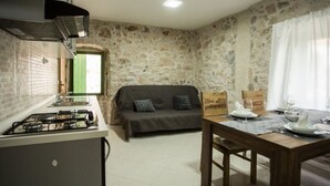 A compact kitchen with a gas stove, a wooden dining table, and a sofa in a stone-walled room. - Apartments Stone House Murter (Murter-Kornati)