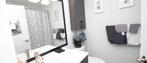 Een moderne badkamer met een wit wastafelmeubel, een grote spiegel, een toilet en een handdoekhouder.